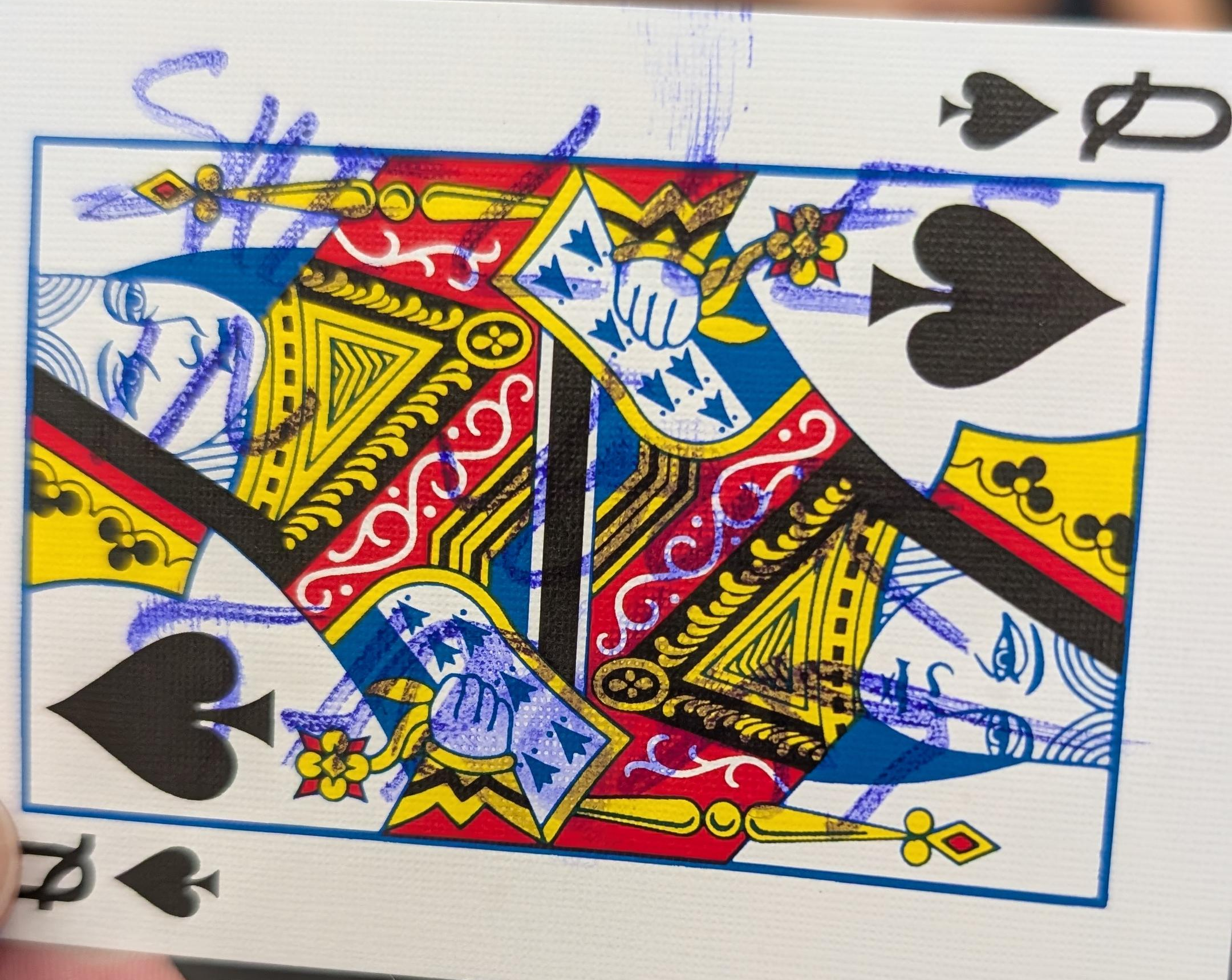 a playing card, the queen of spades, with 'SHE LIVES IN HIS THROAT' scrawled on it in hard to read felt tip pen